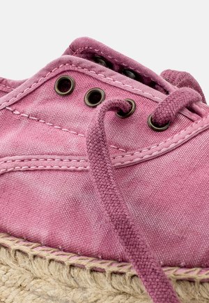 Pink canvas espadrille with round eyelets, textile laces, and a jute rope sole. Features visible stitching and a textured finish.