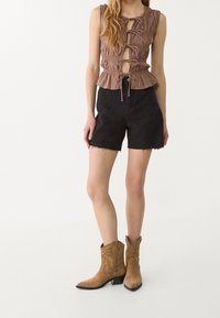 Ruskea, teksturoitu hihaton toppi etutaskuilla, yhdistetty mustiin farkkushortseihin, joissa on raftatut helmat. Kamelin väriset cowboy-kengät, joissa on ommeltuja yksityiskohtia.