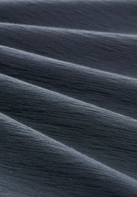 Ciężki szary materiał o teksturowanym wzorze, ukazujący ukośne fałdy i subtelny połysk, wyglądający miękko i zachęcająco.