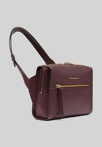 Bolso de cuero burdeos con una forma rectangular elegante, compartimentos dobles con cremallera y herrajes en tono dorado. Cuenta con una correa única y ajustable.