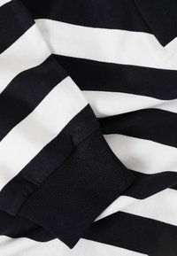Tessuto a righe blu navy e bianche con una finitura текстurizzata. Presenta un polsino a coste e una consistenza morbida e liscia.