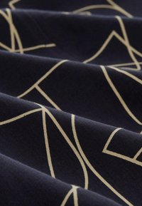 Námořnická tkanina s krémovým geometrickým vzorcem; hladká textura; záhyby vytvářejí hloubku, zdůrazňující kontrast mezi barvami a designem.