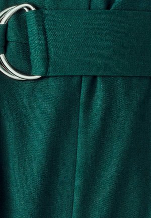 Groene stoffen riem met zilveren dubbele ringgesp op een achtergrond van geplooide groene textuur.