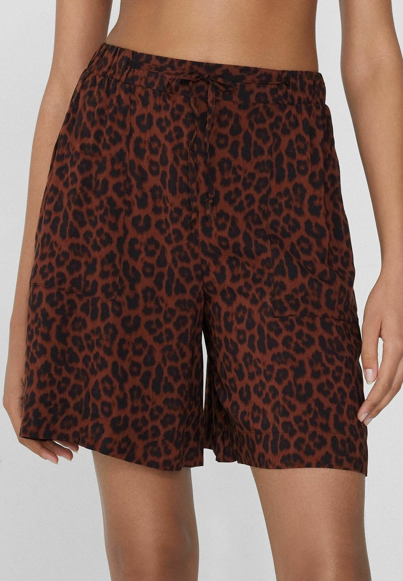 Pantalones cortos marrones con un diseño de estampado de leopardo negro. Presentan una cintura elástica con cordón y bolsillos laterales. Tela suave y ligera.