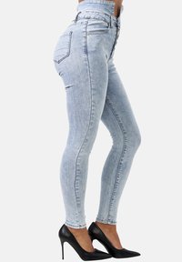 Jeans de mezclilla de tiro alto en azul claro, con un ajuste slim, que presentan un diseño de cinco bolsillos y una textura suave, combinados con tacones altos negros.