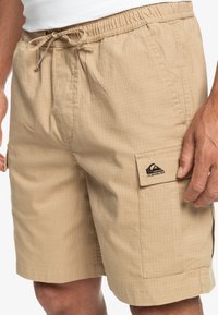 Shorts khaki en tissu texturé, dotés d'une taille élastique avec cordon de serrage, de poches latérales et d'une poche à rabat avec une marque.