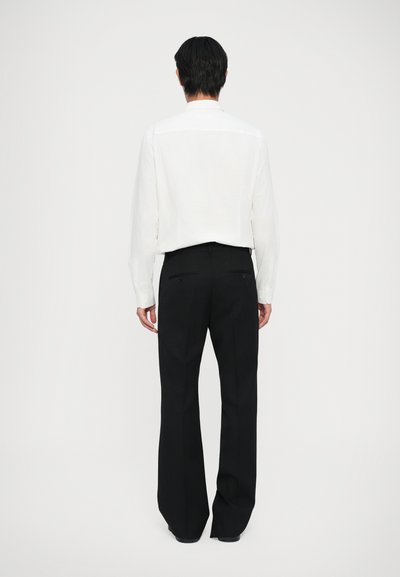 Cămașă albă cu mâneci lungi, cu croială dreaptă și pantaloni negri croiți. Ținuta are un design minimalist și o textură netedă.