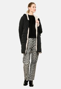 Čierny prešívaný dlhý kabát s krémovým podšívkou, skombinovaný so sivými nohavicami s leopardím vzorom a čiernymi čižmami po členky. Hladká textúra a voľný strih.