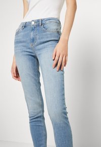 Jeans ajustados de color azul claro, confeccionados en denim, con una cintura de altura media, diseño clásico de cinco bolsillos y un ligero desvanecimiento que añade textura.