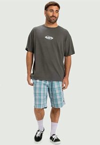 Gray t-shirt with a small blue logo, paired with blue and white plaid shorts, black sneakers, and white socks.