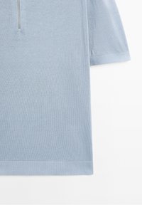 Pull tricoté bleu clair à manches courtes avec une fermeture éclair devant et des bordures côtelées aux manches et à l'ourlet.