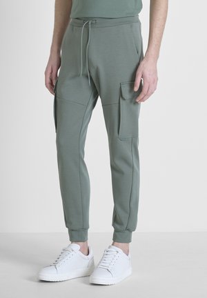 Lichtgroene joggingsbroek met elastische tailleband en trekkoord, voorzien van zijzakken en strakke boorden. Gepaard met witte sneakers.