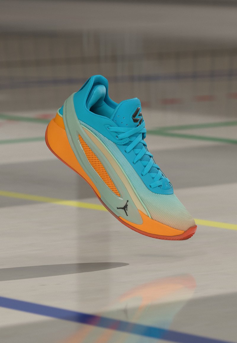 Μπλε και πορτοκαλί αθλητικό παπούτσι στον αέρα πάνω από εσωτερικό γήπεδο με πολύχρωμες γραμμές, με το λογότυπο Jordan στο πλάι.