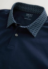 Polo bleu marine avec col à motifs en vagues bleues, deux boutons, taille moyenne, coupe régulière, fabriqué au Sri Lanka.
