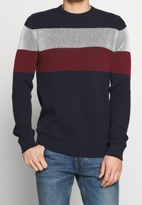 Herrar stickad tröja med marinblå, vit och burgundy horisontella ränder, ribbad textur och rundad halsringning. Tillverkad av ett mjukt tyg.