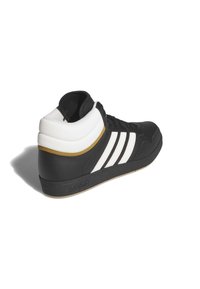 Svart hög sneaker med vita ränder, guldaccent, strukturerad gummisula och vadderad krage för stöd.