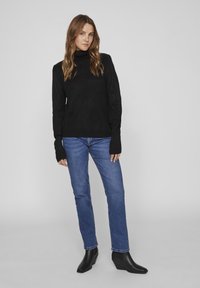 Svart stickad polotröja med långa ärmar, kombinerad med blå jeanstyg. Modellen har på sig svarta klackade ankelstövlar. Enkelt, rent design.