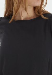 Top blu scuro con scollatura rotonda, tessuto morbido e maniche corte con un delicato dettaglio arricciato sulle spalle.