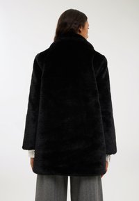 Czarny płaszcz z sztucznego futra z wysokim kołnierzem, długimi rękawami i luźnym krojem. Tekstura wydaje się miękka i puszysta, zaprojektowana z myślą o cieple.
