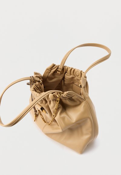 Μπεζ δερμάτινη γυναικεία τσάντα με μαζεμένη κορυφή, λεπτές τιράντες, χρυσή αλυσίδα διακόσμηση και ανοιχτό εσωτερικό που δείχνει μια τσέπη με φερμουάρ και ετικέτα.