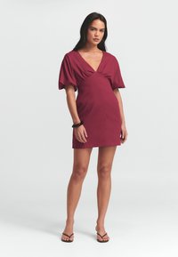 V-paita, lyhyet puffihihat ja tiukka siluetti, vadelmanvärinen mekko. Sujuva kangas minimalistisella suunnittelulla. Tasapohjaiset sandaalit jalassa.