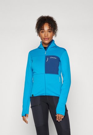 Veste zippée bleue avec un motif texturé, dotée d'un panneau bleu marine sur la poitrine, de poches latérales et d'ouvertures pour les pouces sur les manches.