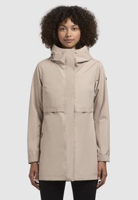 Beige waterdichte jas met een hoge kraag, rits aan de voorkant en een grote klepzak. Het heeft lange mouwen en een relaxte pasvorm.