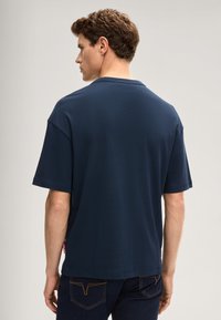 Granatowy bawełniany t-shirt z krótkimi rękawami, okrągłym dekoltem i luźnym krojem, z małą metką marki po lewej stronie.