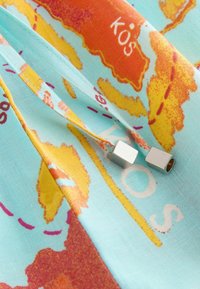 Close-up of light blue fabric printed with orange and yellow map details labeled "KOS" and two silver cube-shaped cord ends.