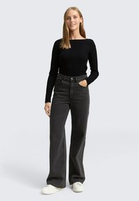 Zwarte geribbelde top met lange mouwen gecombineerd met hoge taille, wijde antracietkleurige jeans; model draagt witte sneakers, eenvoudig ontwerp, geen patronen.