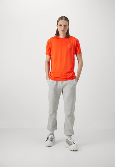Lys orange kortærmet træningsskjorte med rund hals og et lille grafisk detalje; parret med lysegrå joggingbukser og chunky sneakers.
