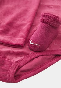 Fukcija Nike oblačilni set, ki vključuje mehak, teksturiran top in ujemajočo se nogavico s prepognjenim robom ter belim logotipom.