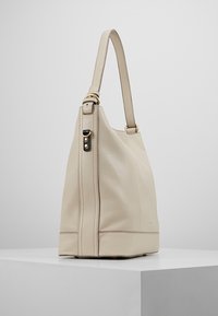 Beige läderhandväska med en rymlig design, som har ett enda band och detaljer i guldfärgade accenter. Mjuk textur och strukturerad form.