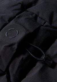 Tela negra con una textura suave, que presenta un logotipo circular y un cordón con un tope de plástico para ajuste.