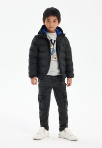 Black puffer jacket with a blue-lined hood, gray graphic sweatshirt, dark cargo pants, and white sneakers; features a quilted texture.