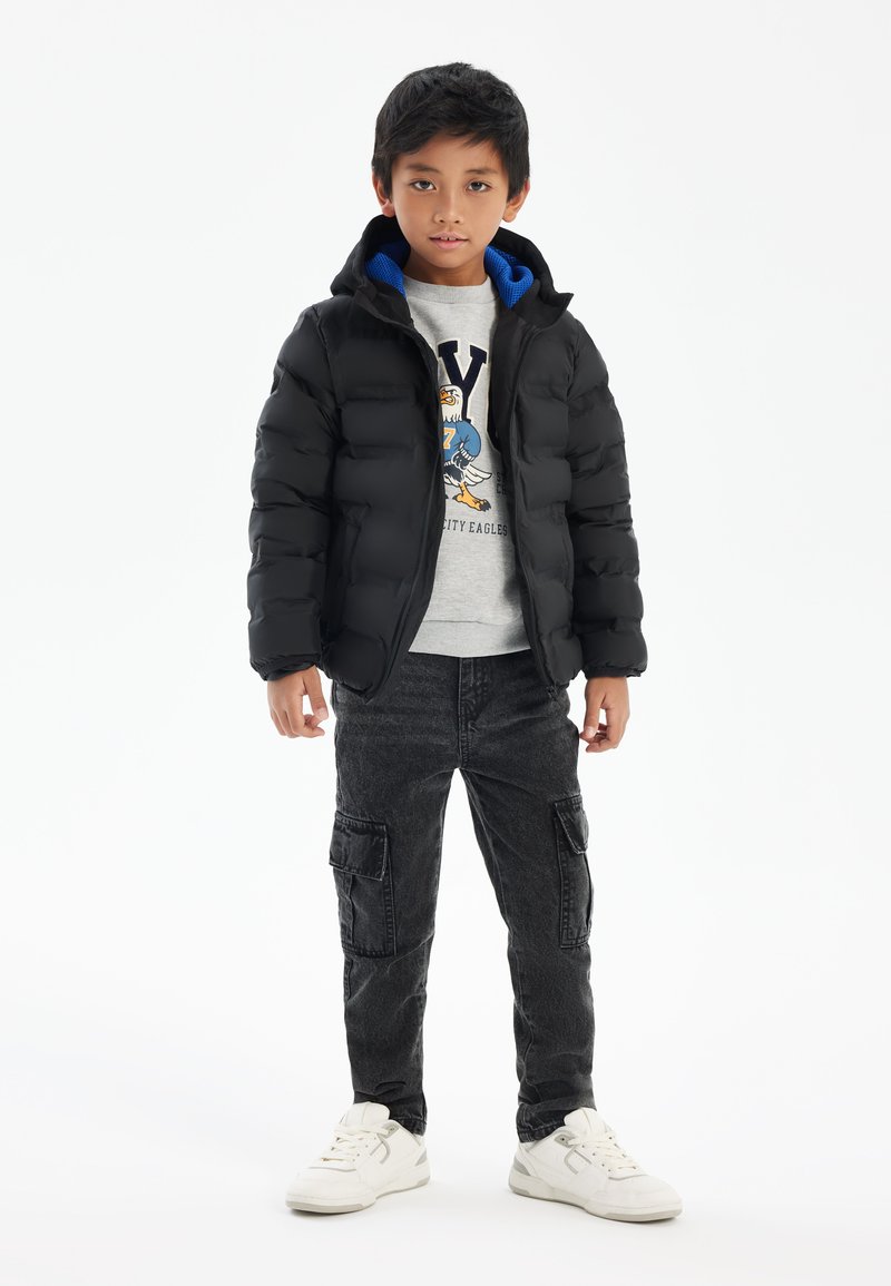 Black puffer jacket with a blue-lined hood, gray graphic sweatshirt, dark cargo pants, and white sneakers; features a quilted texture.