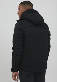 Black insulated jacket with a hood, featuring a zip closure, side pockets, and a smooth texture. The design is minimalistic and functional.