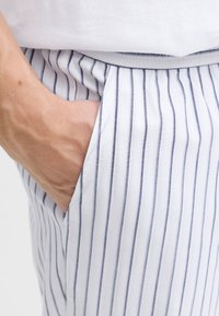 Witte stoffen broek met smalle marineblauwe strepen, voorzien van een zijzak en een comfortabele tailleband, getoond in een close-up weergave.