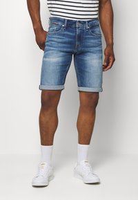 Jeansshorts i ljusblått med en urblekt finish och uppvikt fåll, kombinerat med vita sneakers och vita strumpor. Randig t-shirt syns ovanför.