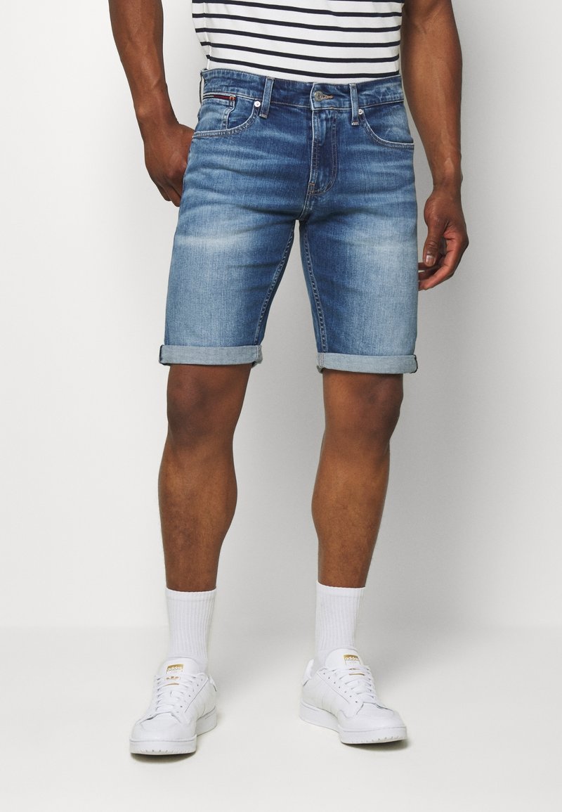 Jeansshorts i ljusblått med en urblekt finish och uppvikt fåll, kombinerat med vita sneakers och vita strumpor. Randig t-shirt syns ovanför.