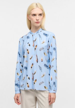 Blusa azzurro chiaro con colletto alla mandarina, caratterizzata da una stampa astratta di piume in vari colori. Maniche lunghe con polsini arricciati, texture liscia.