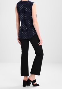 Marinblå ärmlös blus med vita prickar, rundad nederkant, ihop med svarta utsvängda byxor och svarta klackar. Enkel design, slät tyg.