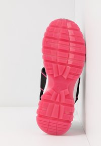 Semelle de chaussure avec une bande de roulement rose vif, taille 37, marquée Marc Cain, positionnée verticalement contre un mur d'angle blanc.