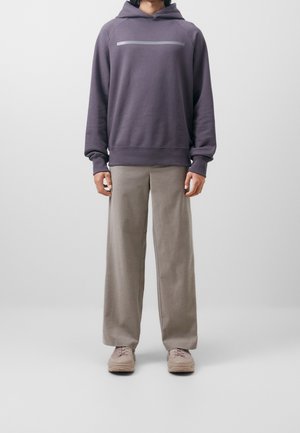 Person wearing a purple hoodie, beige wide-leg pants, and beige sneakers, standing against a plain light gray background.
