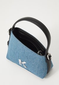 Bolsa de ganga com uma alça de pele escura, forma triangular, logótipo prateado e interior com fecho. Apresenta um exterior de tecido texturizado azul.