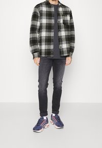 Svart och vit rutigt flanellskjorta över en mörk t-shirt, i kombination med mörka jeans och blåa sportskor med rosa detaljer.