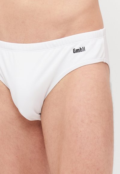 Caleçons de bain blancs en tissu lisse, avec une coupe taille basse et un logo "GmbH" noir subtil sur la ceinture.