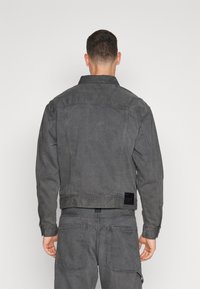 Γκρι τζην μπουφάν με γιακά, μανίκια με κουβέντα και πλαϊνές τσέπες. Περιέχει μια μαύρη ταμπέλα στην πλάτη για branding.