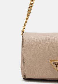 Béžová kožená kabelka s texturovaným povrchem, která má zlatou řetízkovou výstuhu a trojúhelníkový logo akcent na přední straně.