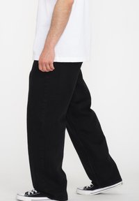 Sorte denimbukser med en løs pasform, der har høj talje og lige ben. Båret med en hvid t-shirt og sorte sneakers.